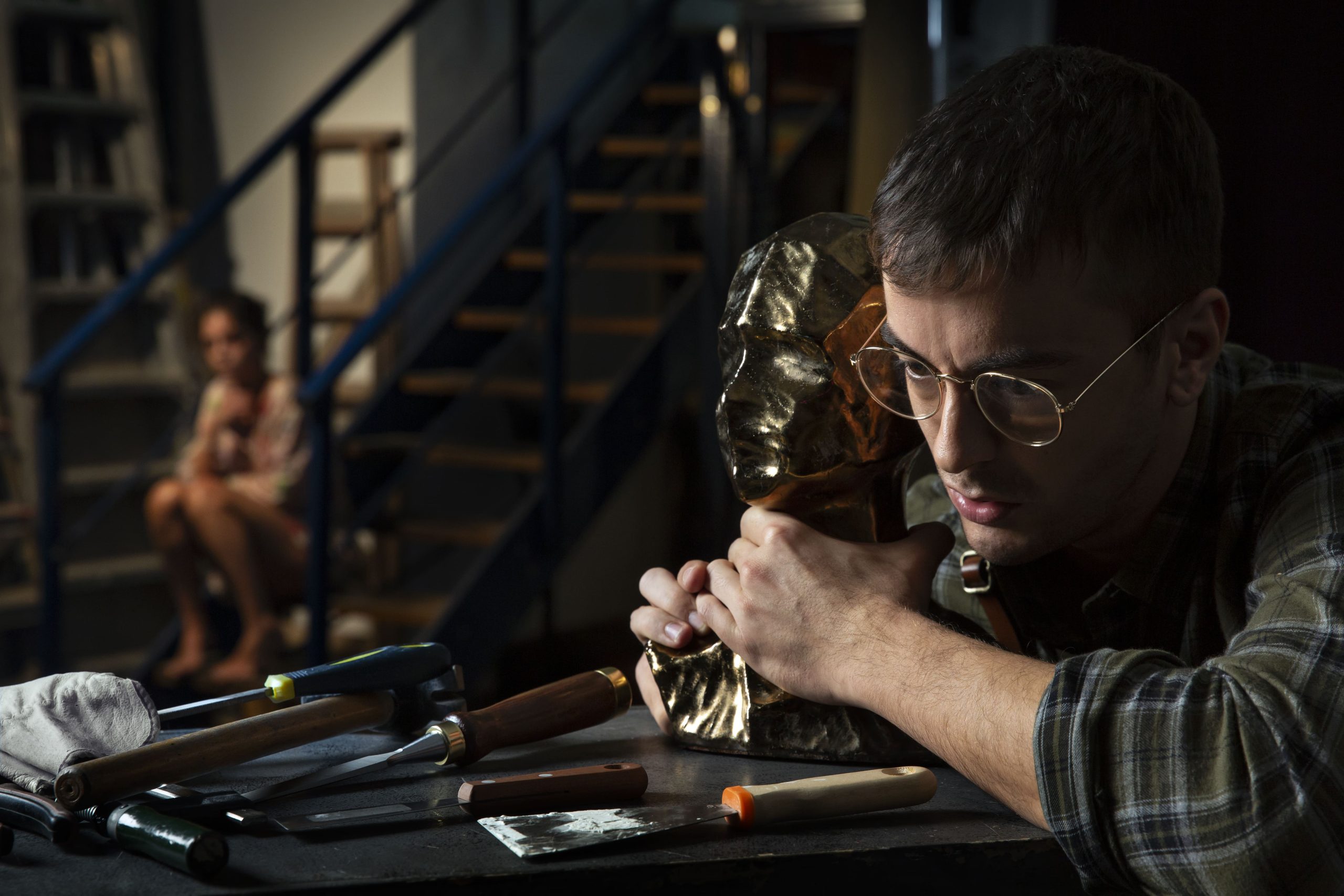 Foto de El Monstruo de White Roses. Un hombre con gafas agarrando un trofeo y una chica en el fondo sentada en las escaleras